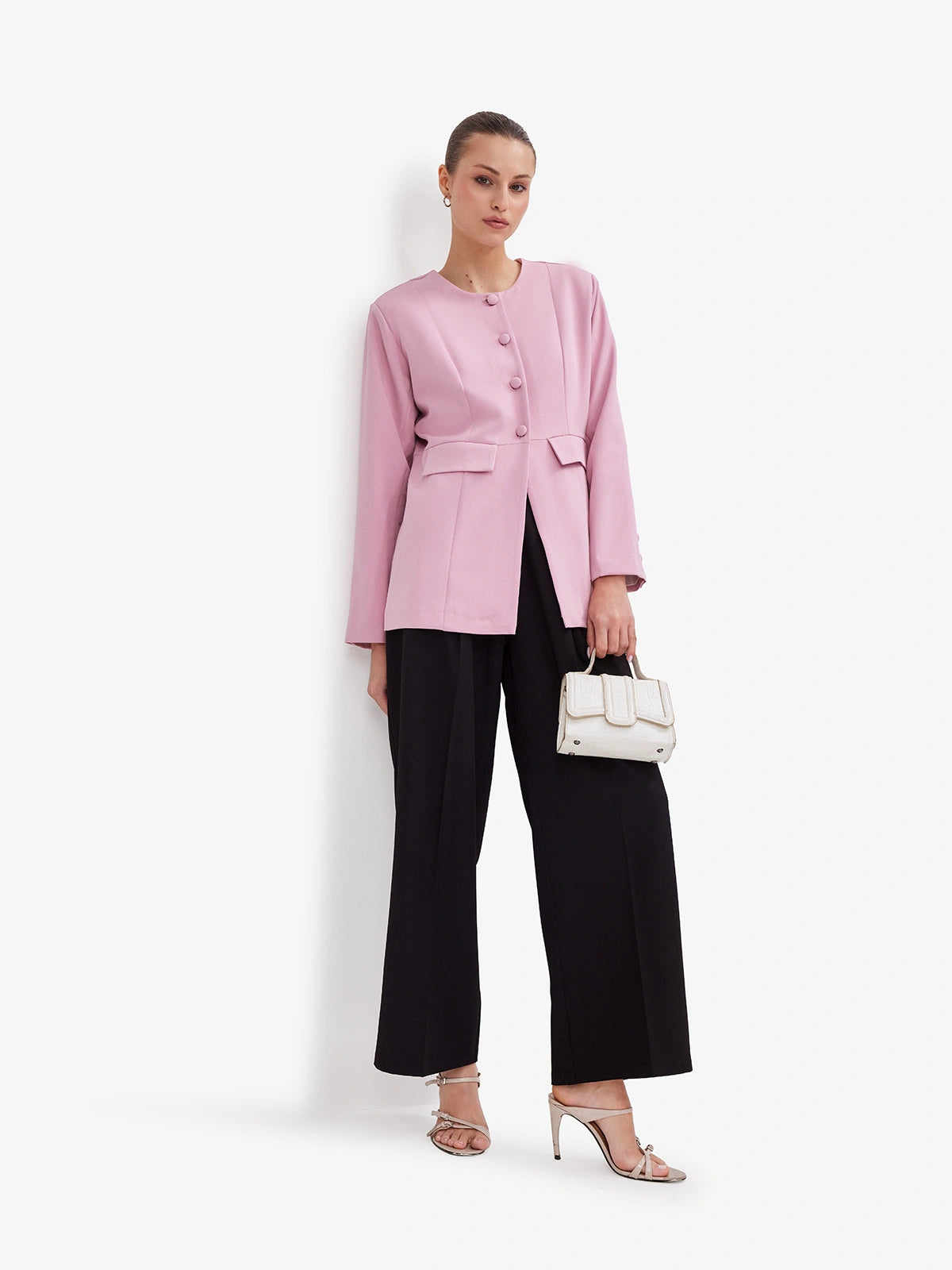 Woman wearing a pink blazer and black pants with a white handbag on a white background