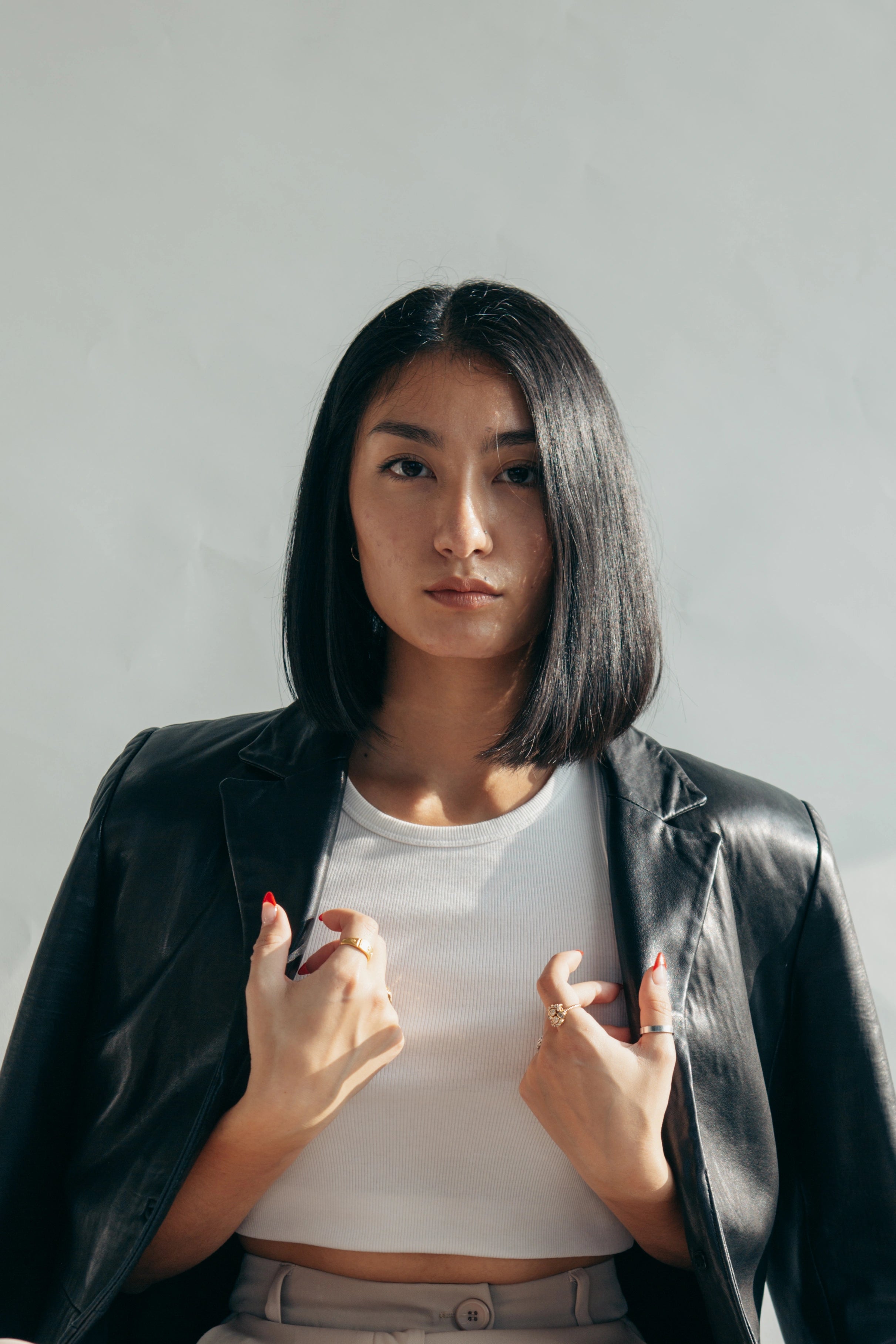 Woman wearing a black leather jacket over a white top against a plain background