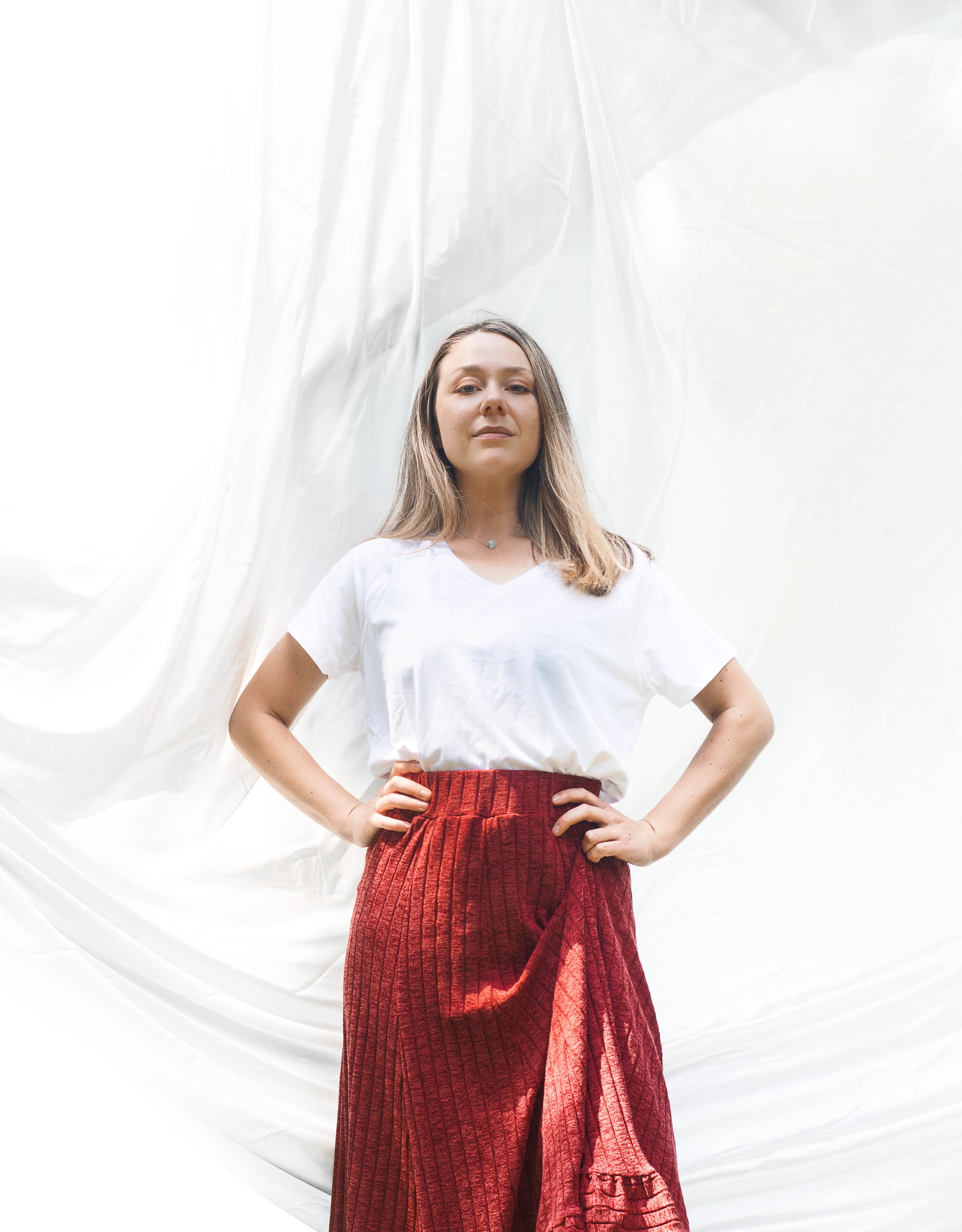 Woman wearing a white top and red skirt against a white curtain background